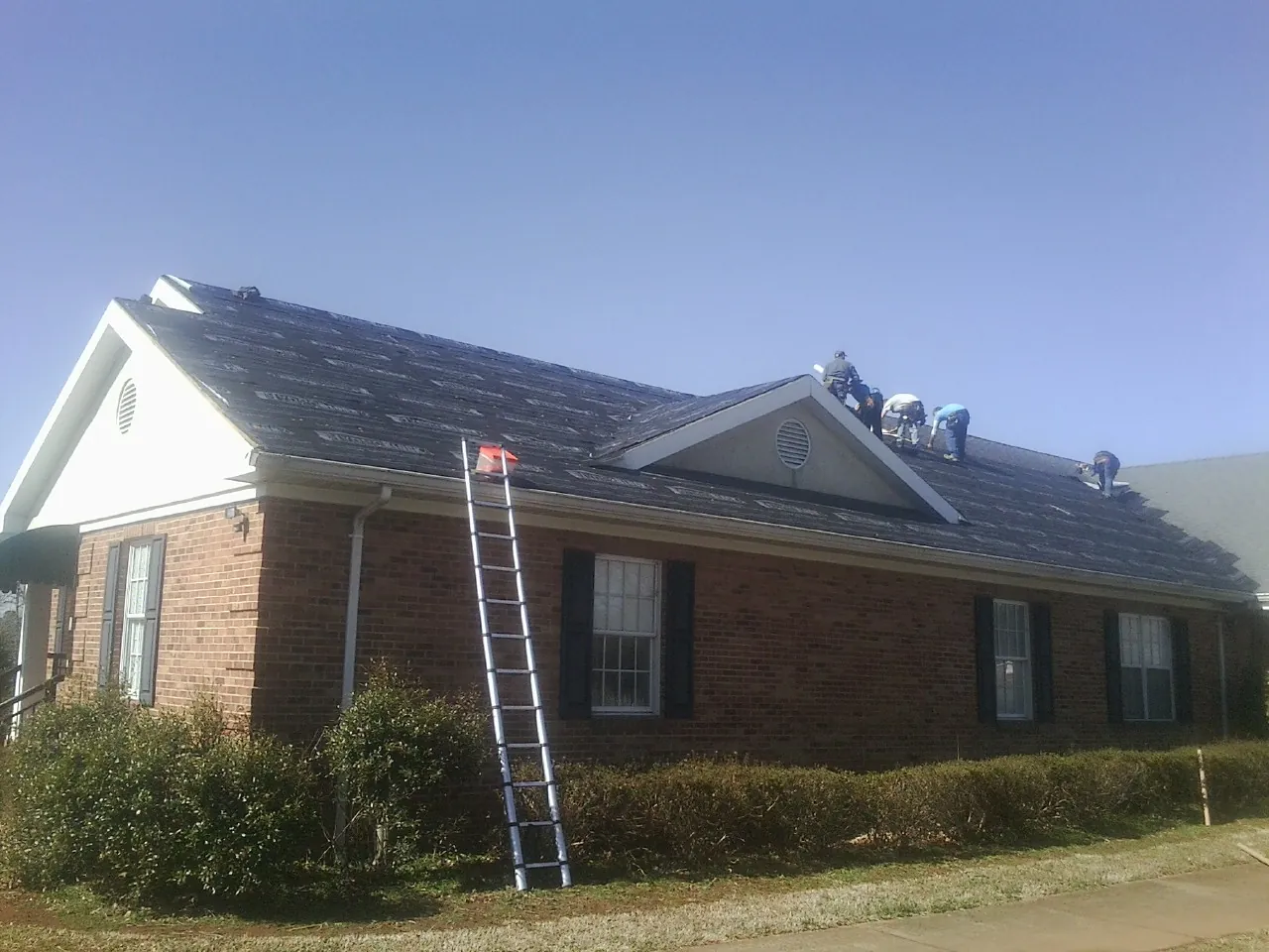 Crew tearing shingles off a brick ranch roof with a ladder set — Emergency Roof Repair work by our crew in Winder