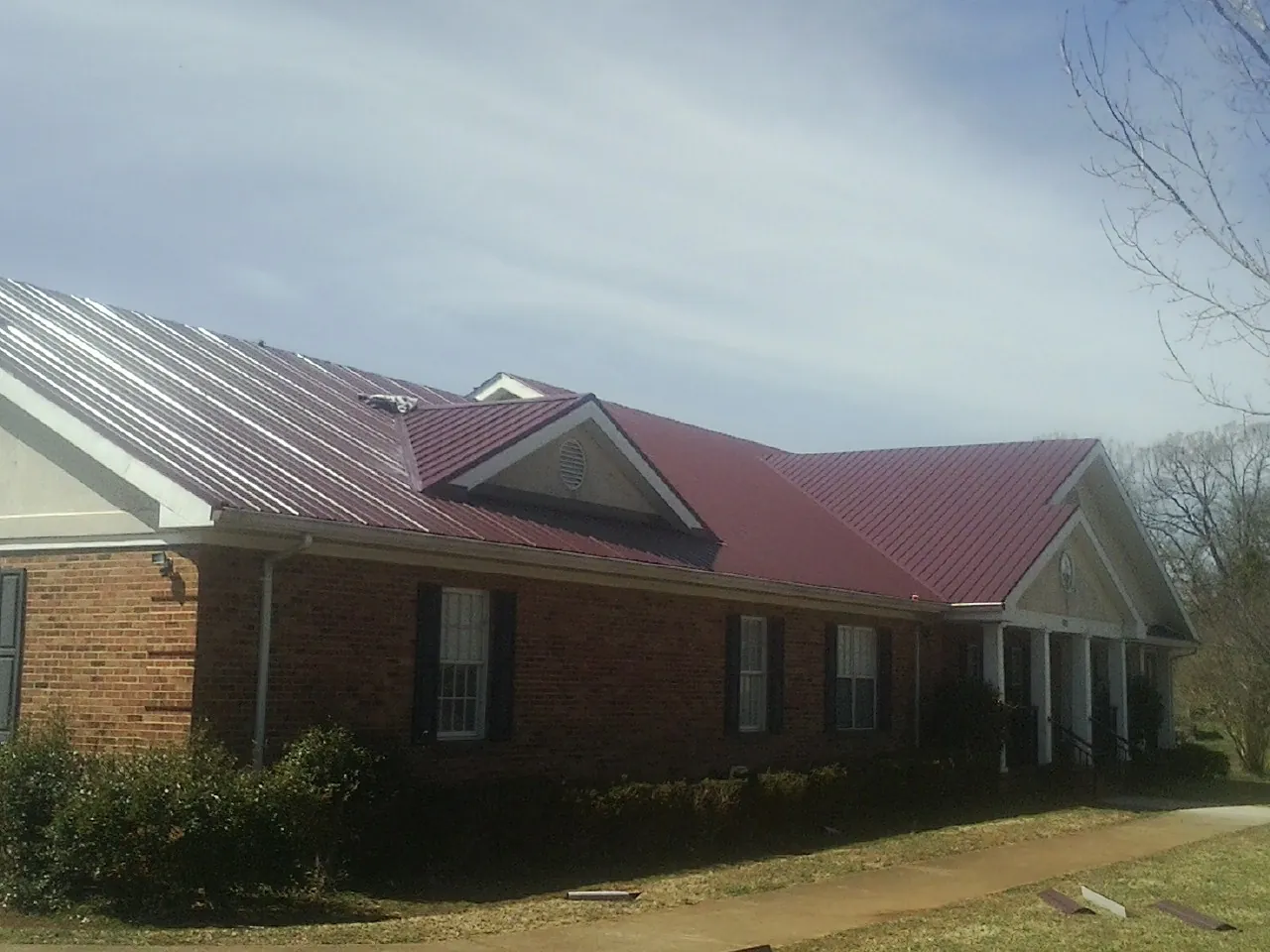 Red metal roof with gabled entries on a long brick building, from a Hail Damage Roof Repair job in Winder