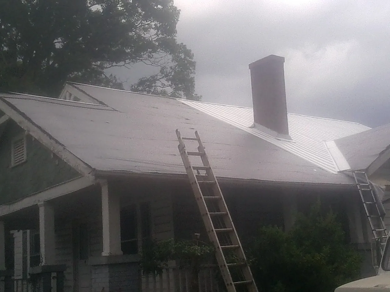 Ladders against a metal roof on an older home with a brick chimney in Winder