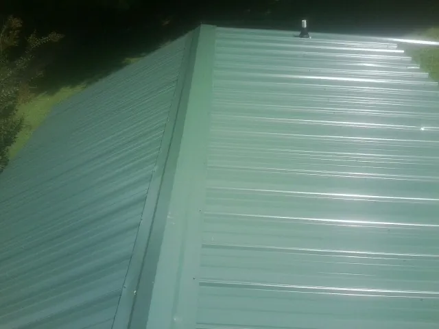New green metal panels meeting at the ridge of a roof — Flat Roof Repair work by our crew in Winder
