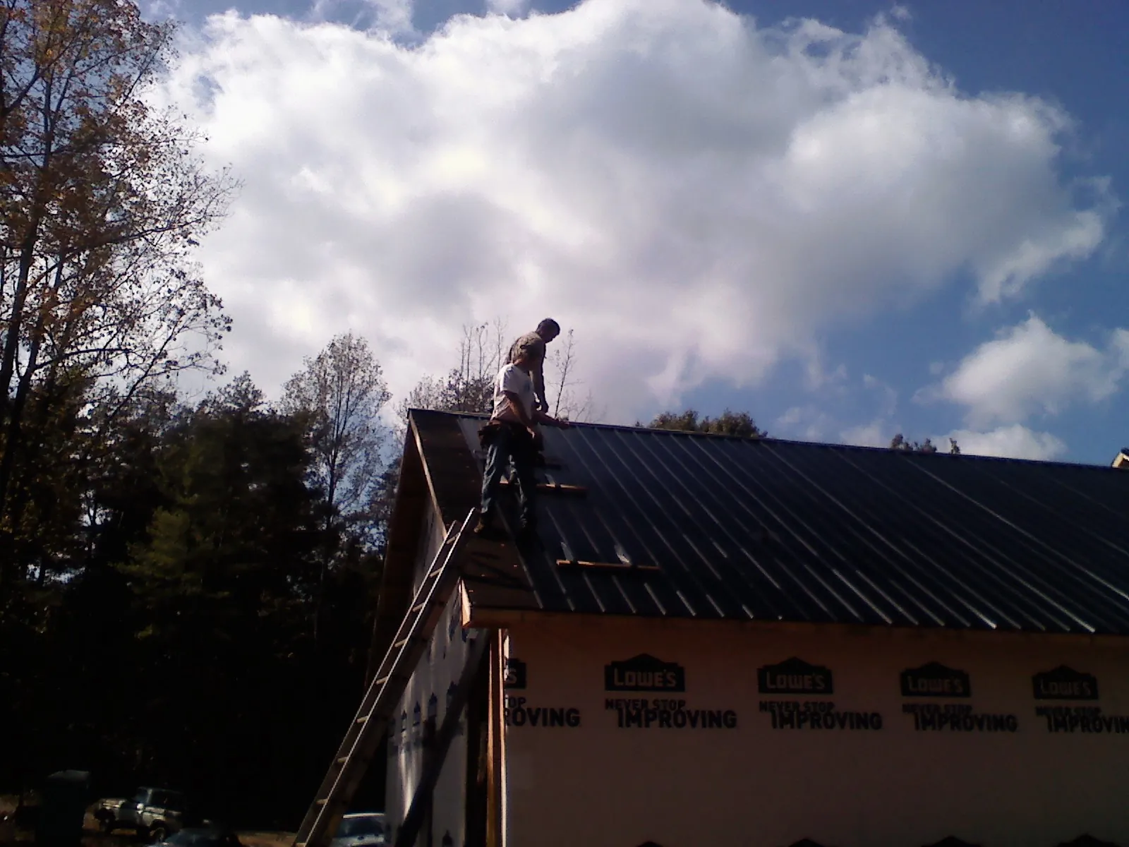 Roofer fastening dark metal panels high against a cloudy sky, from a Roof Inspection job in Winder