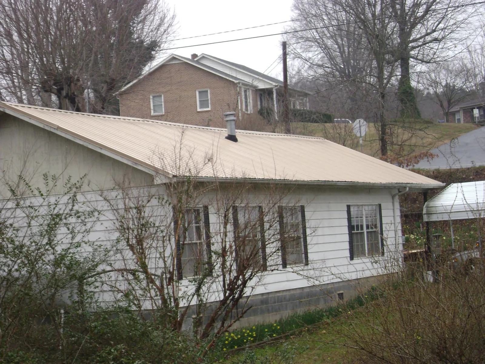 Tan metal roof on a white sided house set into a hillside — Commercial Roofing by Roofing Brothers in Winder